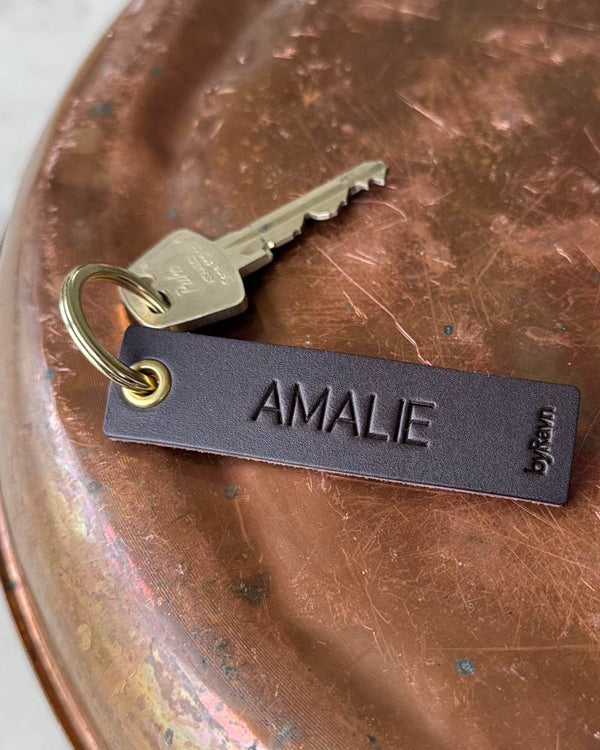 SOLO Small Schlüsselanhänger aus dunkelbraunem Leder mit dem gravierten Namen "Amalie", goldfarbenem Ring und Schlüssel auf Kupfertablett