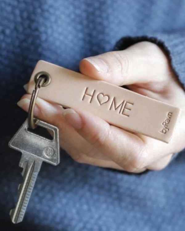 SOLO Small Schlüsselanhänger aus naturfarbenem Leder, in der Hand gehalten, mit Schlüssel und der Gravur "Home" mit Herz als O