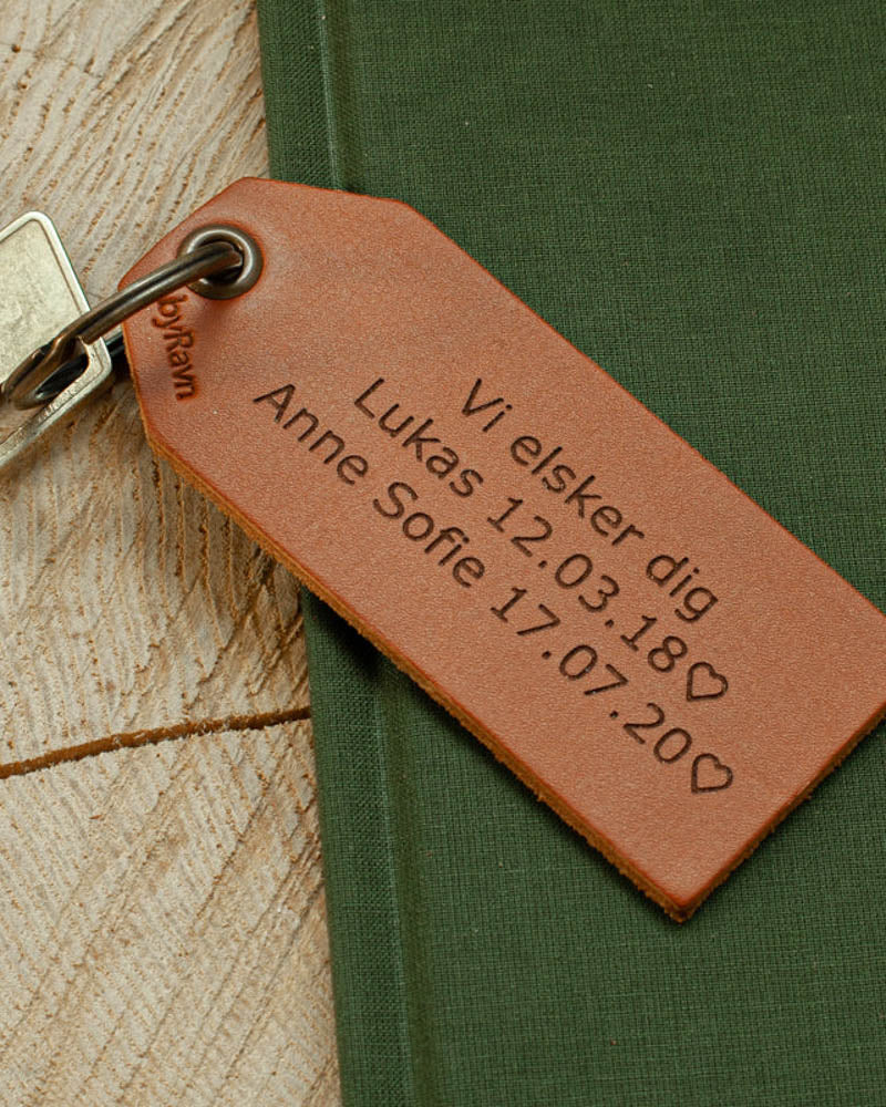 STORM Schlüsselanhänger aus Leder in Cognac mit persönlicher Gravur "Vi elsker dig, Lukas 12.03.18 ♡ Anne Sofie 17.07.20 ♡" auf grünem Buch