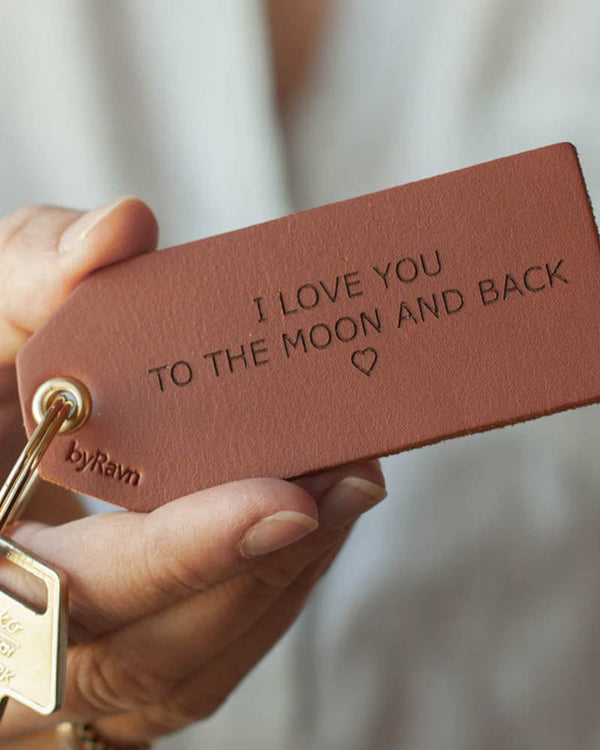 STORM Schlüsselanhänger aus Leder in Cognac, in der Hand gehalten, mit Schlüssel und der Gravur "I love you to the moon and back" ♡