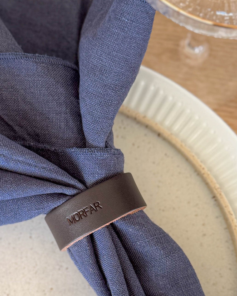 KNOT Serviettenring Tischkarte aus dunkelbraunem Leder mit der Gravur "Morfar" um dunkelblaue Leinenserviette auf geriffeltem Teller