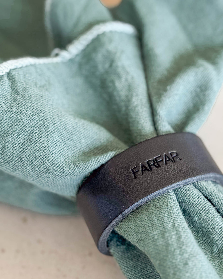 KNOT Serviettenring aus schwarzem Leder mit der Gravur "Farfar" um hellgrüne Stoffserviette