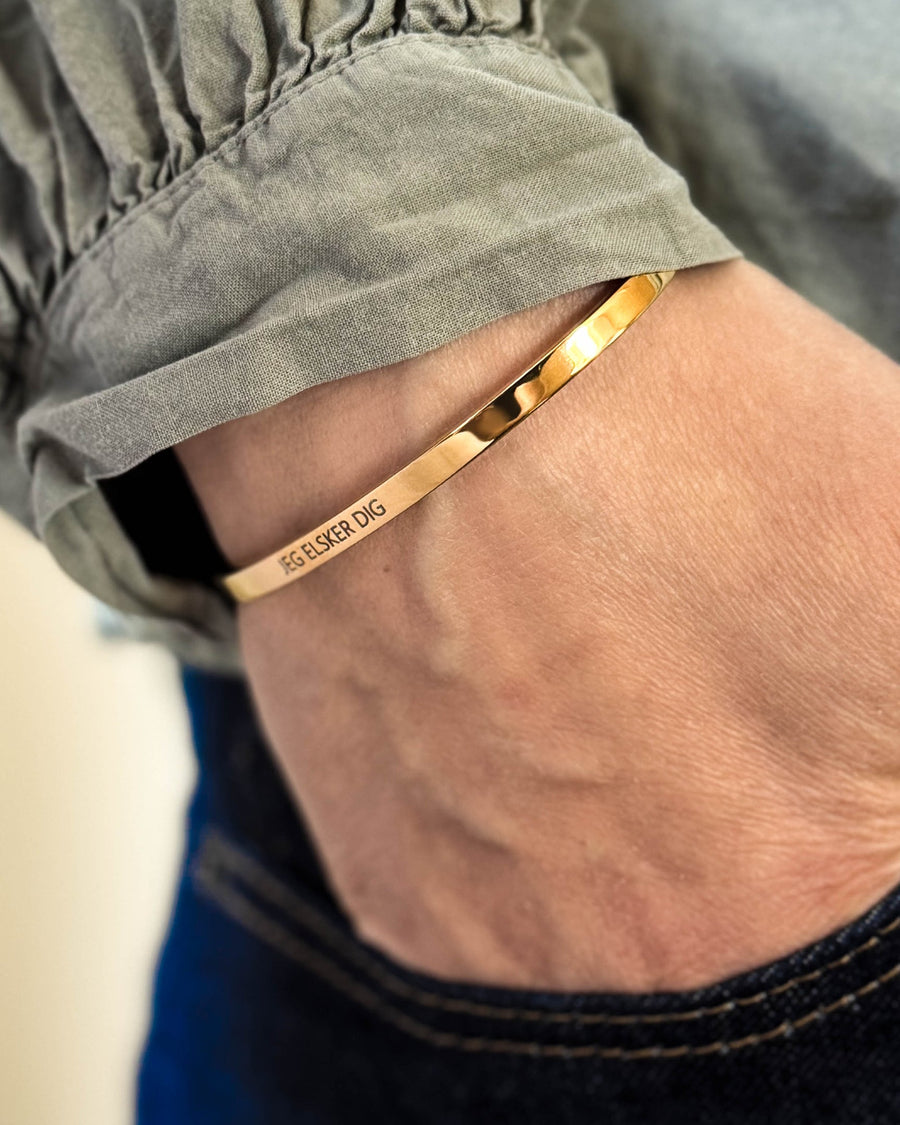 VENUS Armband aus vergoldetem Edelstahl mit der Gravur "Jeg elsker dig" am Handgelenk, Hand in der Tasche dunkler Jeans