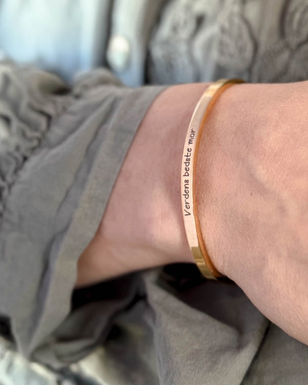 VENUS SCRIPT Armband aus vergoldetem Edelstahl mit "Verdens bedste mor" in Handschrift am Handgelenk, graue Bluse