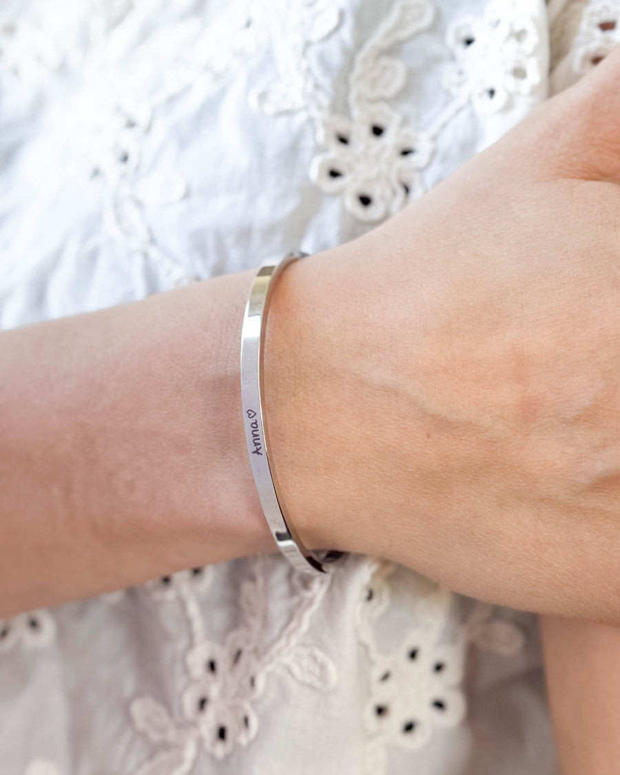 VENUS SCRIPT Armband aus silberfarbenem Edelstahl mit dem Namen "Anna" ♡ in Handschrift am Handgelenk, weiße bestickte Bluse