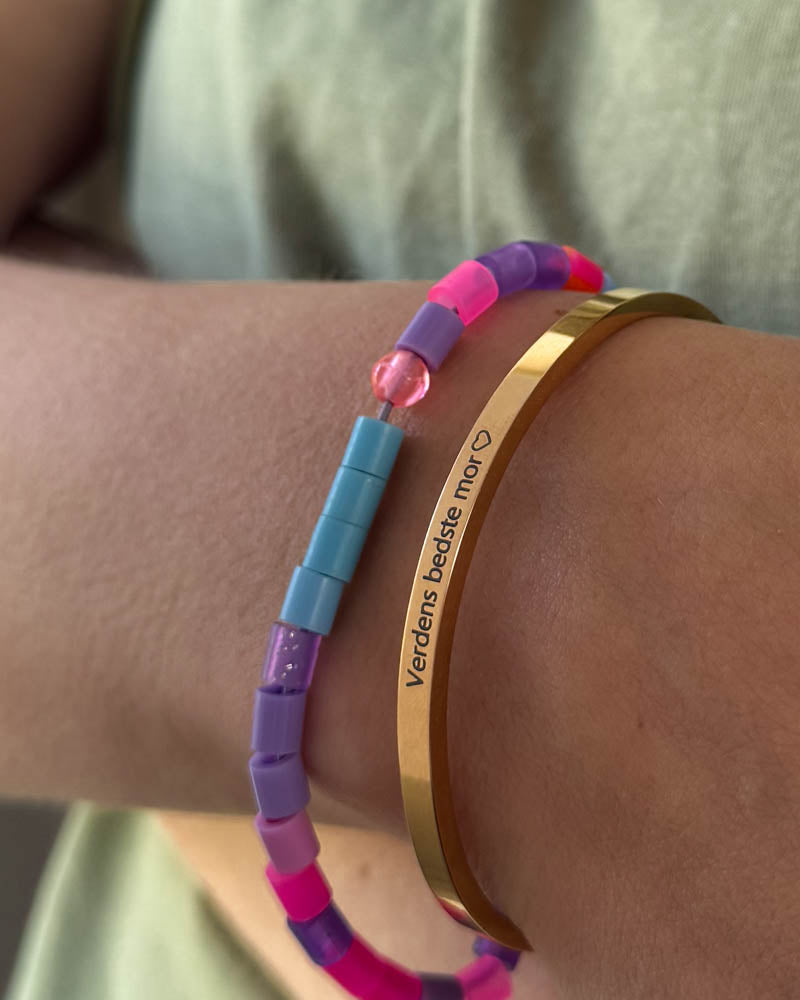 VENUS Armband aus vergoldetem Edelstahl mit der Gravur "Verdens bedste mor" ♡ getragen mit buntem Perlenarmband