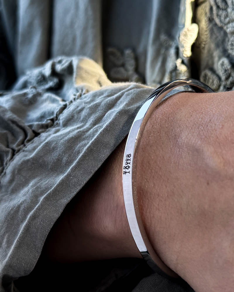 VENUS STICK Armband aus silberfarbenem Edelstahl mit gravierter Streichholz-Familie, getragen zu grauer Bluse mit Puffärmeln