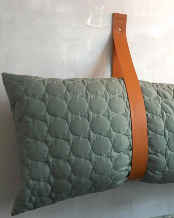WAVE Lederschlaufe aus cognacfarbenem Leder an der Wand montiert als Halter für grünes gestepptes Kissen neben Bank