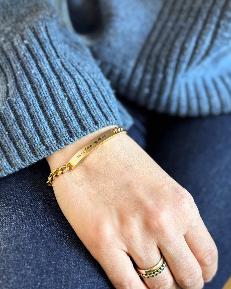 ZOE Namensarmband aus vergoldetem Edelstahl mit "Merle, Esther og Vilhelm" graviert, am Handgelenk, blauer Strick und Jeans